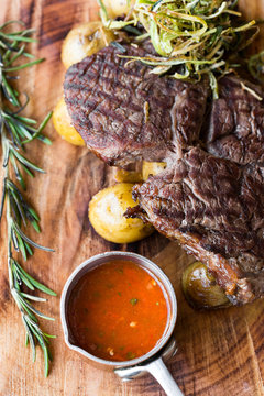 Top view of grilled ribay steak with potatoes, vegetables and sauce on a wooden plate. close-up