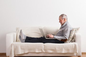 Senior man sitting on sofa, working on laptop.