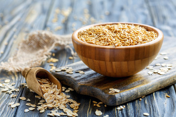 Whole oats in a bowl and oat flakes in a wooden scoop.