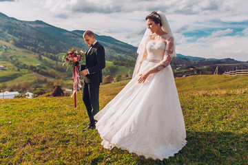 Beautiful bride and groom at the mountains. Newlyweds dancing and walking on fileld. Copy space.
