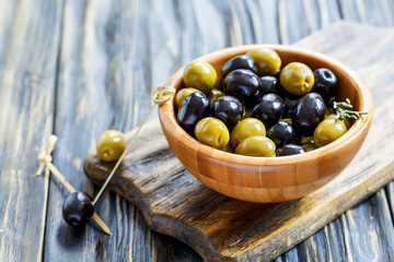 Black and green olives in a bowl and bamboo skewer.