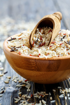 Different varieties of rice and a wooden scoop in a bowl.