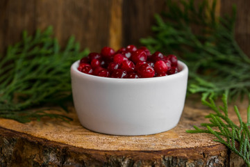 Pickled cranberries in a sweet syrup in a white bowl on the wooden background with the leaves of juniper