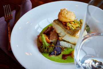 White stewed pikeperch fish in green pesto sauce with vegetables for steaming broccoli, carrots, beets, mushrooms, mashed potatoes , there is a glass with clean water