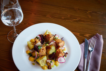 Baked potato slices and beets with vegetables and roast pork bacon on dark wooden table served in restaurant interior