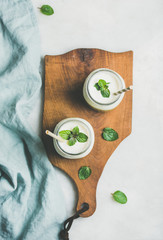 Ombre layered green smoothies with mint in glass jars with straws on wooden board over light grey background, top view. Clean eating, vegan, vegetarian, weight loss, healthy, diet food concept