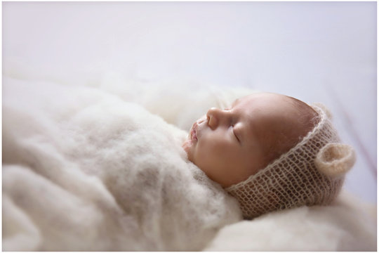 A small baby is dressed in white and covered with a blanket and he is peacefully sleeping during his first photoshoot.
