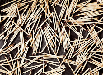 Many wooden household safety matches with brown heads lying chaotically on a black background