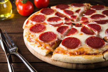 Sliced italian Pepperoni pizza with salami on dark wooden background close up. Italian traditional food. Popular street food.
