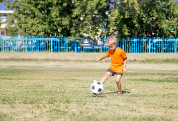 little boy in orange shirt playing soccer, kicking the ball