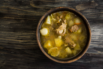 Soup with meat in a wooden bowl on a wooden table. Tasty and nutritious dish.