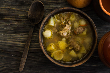Soup with meat in a wooden bowl on a wooden table. Tasty and nutritious dish.