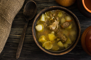 Soup with meat in a wooden bowl on a wooden table. Tasty and nutritious dish.