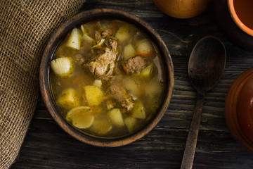 Soup with meat in a wooden bowl on a wooden table. Tasty and nutritious dish.