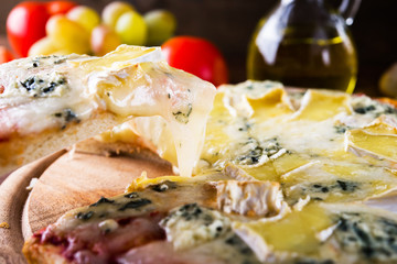 Slice of italian cheesy pizza with different sorts of cheese on dark wooden background. Italian traditional food. Popular street food.