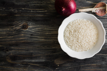 Raw rice in a white bowl on a wooden table and ingredients