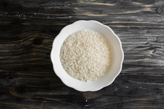 Raw rice in a white bowl on a wooden table