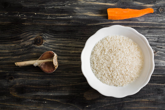 Raw rice in a white bowl on a wooden table and ingredients