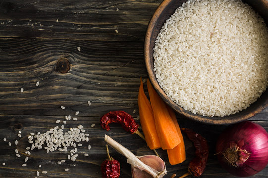 Raw rice in a wooden bowl on a wooden table and ingredients