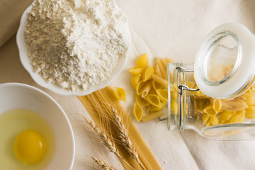 Raw pasta on a white sacking and ingredients. Different types of pasta.