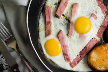 Fried eggs with ham in a frying pan on a wooden table in rustic style