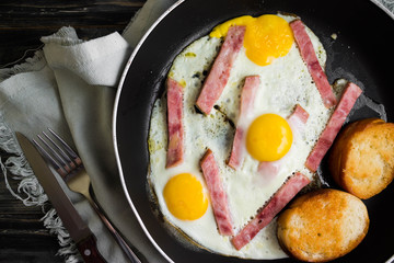 Fried eggs with ham in a frying pan on a wooden table in rustic style