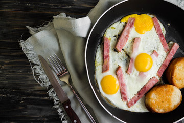 Fried eggs with ham in a frying pan on a wooden table in rustic style