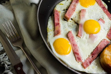 Fried eggs with ham in a frying pan on a wooden table in rustic style