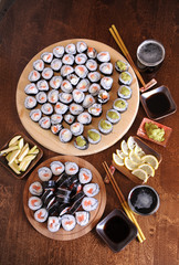 Homemade sushi rolls. Sticks, lemon, soy sauce, wasabi are served on a dark brown wooden table