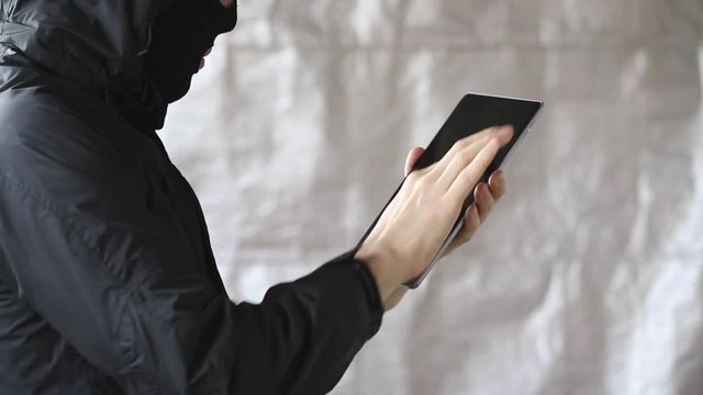 Hacker hacks tablet. The person in the mask receives secret information.