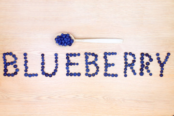 Healthy food. Word "blueberry" made of  berries and wooden spoon isolated on beige background