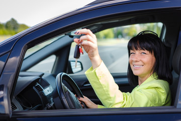 Happy smiling brunette woman 35 years old with car key in hand sitting In The Driver's Seat of Her Car with spring-summer mood. Woman Driving. Dressed in green jacket with sun glasses on head