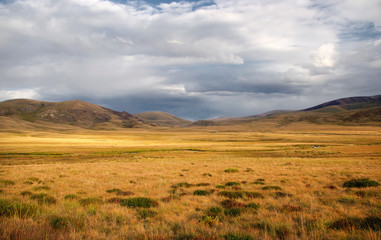 A wide valley steppe with yellow grass under a cloudy sky on the background of mountain ranges, the...