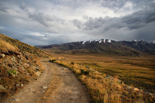 Extreme rocky road in a mountain valley to the pass in cloudy weather on the background of snowy mountain ranges Plateau Ukok Altai Siberia Russia