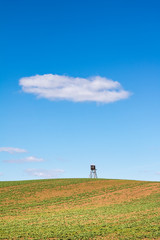 Spring landscape with field, hunting hide and blue sky