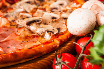 Italian traditional food. Fresh pizza with tomatoes, ham, mushrooms, cheese and parsley on wooden table, close up view.