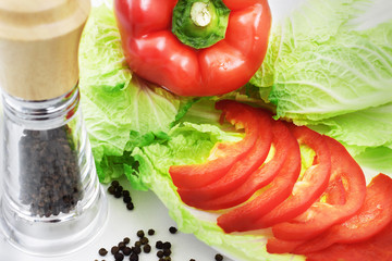 Fresh vegetables (paprika, green salad), scented peppercorns and pepper mill on white background