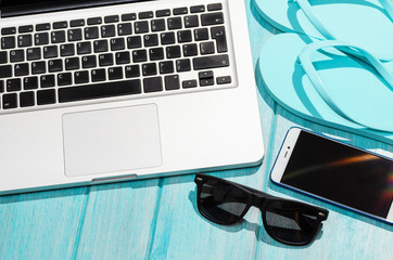 Work on the go. Modern laptop computer with smartphone and sunglasses on blue table, view from above