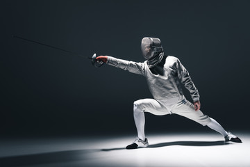 Professional fencer in fencing mask with rapier standing in position on grey - obrazy, fototapety, plakaty