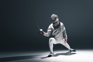 Professional fencer in fencing mask with rapier standing in position on grey - obrazy, fototapety, plakaty