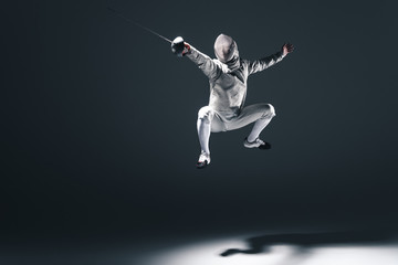 Professional fencer in fencing mask with rapier jumping on grey - obrazy, fototapety, plakaty