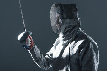 Portrait of professional fencer in fencing mask with rapier on grey
