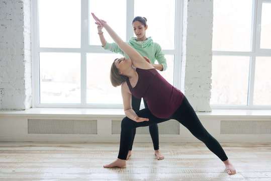 Personal yoga instructor assisting pregnant woman student