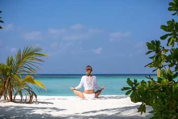 Young beautiful woman meditation on beach Maldives