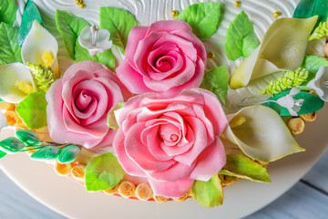 Delicious cake with roses, lily and leaves on light blue wooden table close up with selective focus
