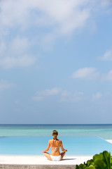 Beautiful girl sits in a pose of a lotus and meditates on the coast Maldives
