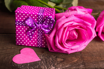 Pink roses and a gift on a wooden background