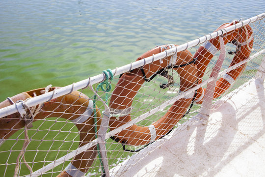 Three lifebuoy on ferry board with green river waters at bottom