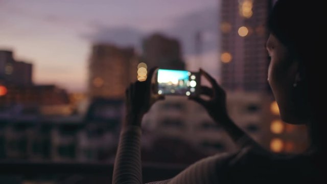 Closeup of woman taking photo of cityscape view with smartphone in bar rooftop terrace at night