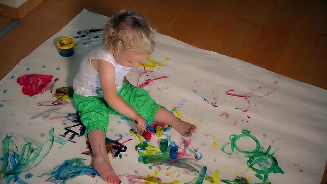 young artist kid girl painting on her hand and white paper on floor